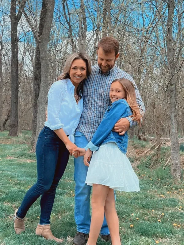 A happy family of three embracing outdoors in a natural setting.