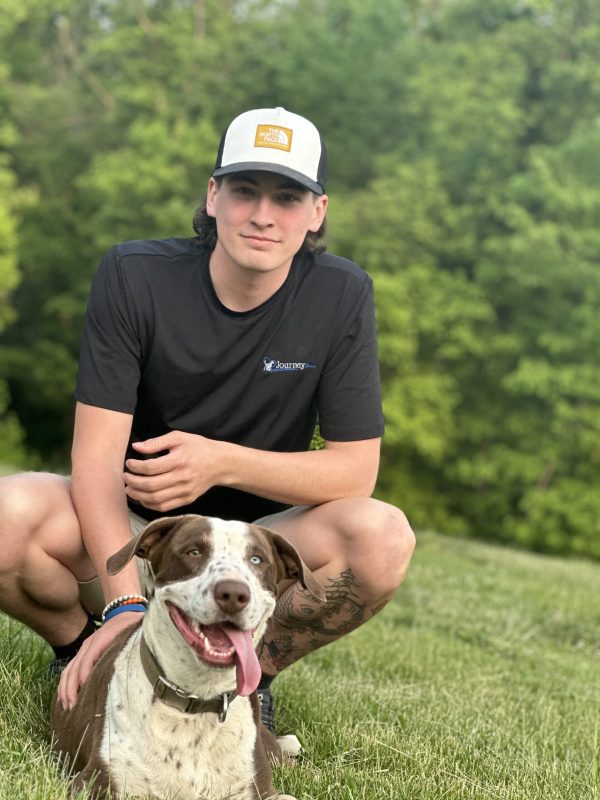Young man in a cap sitting on grass with a happy dog.